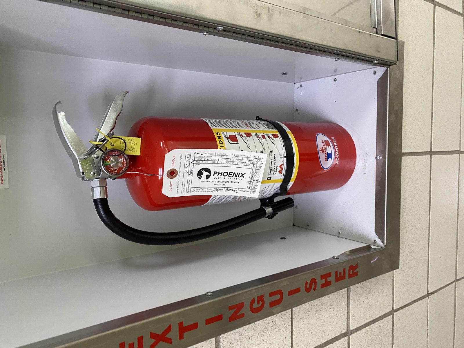 Red Badger fire extinguisher in a wall cabinet with a Phoenix Fire & Systems inspection tag