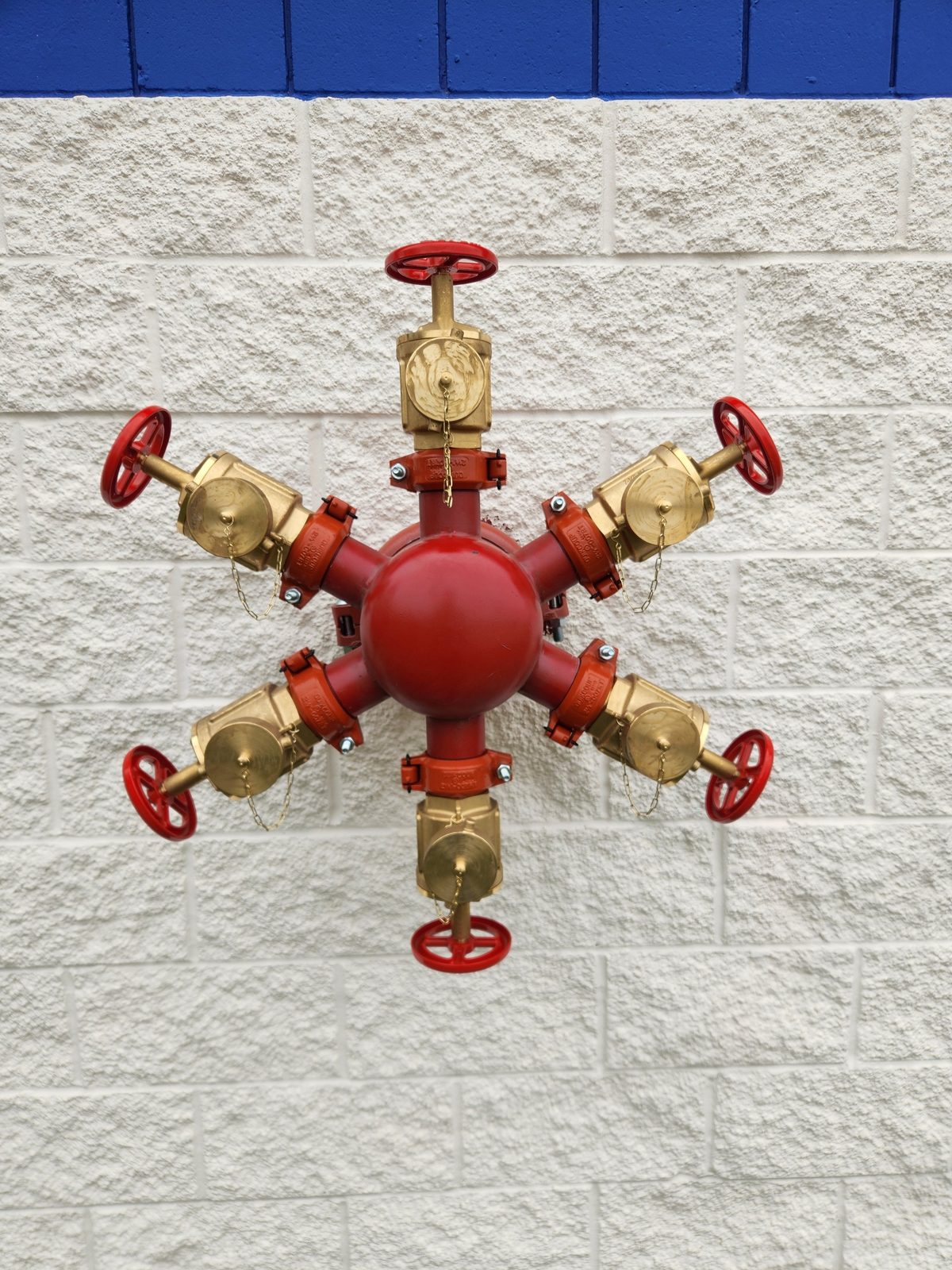 Six-way fire department connection manifold on a white block wall