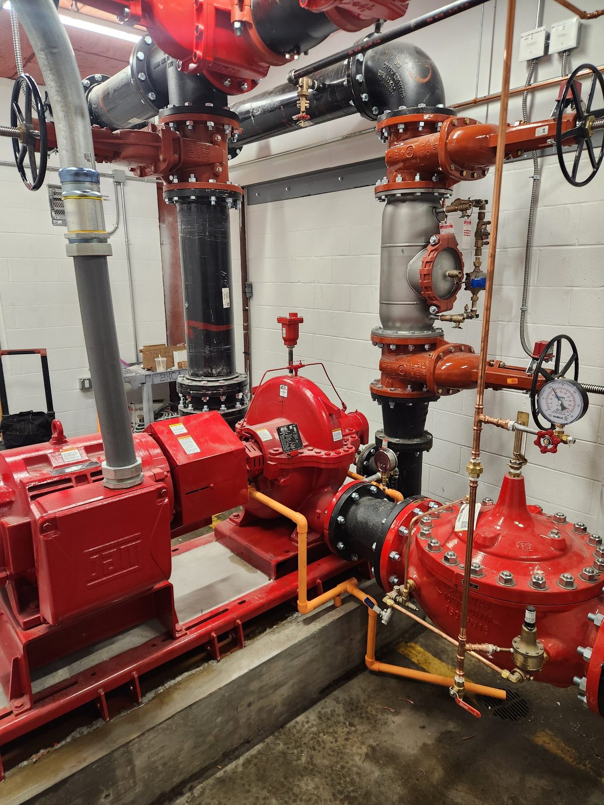 Red electric fire pump, motor, and risers in a commercial pump room